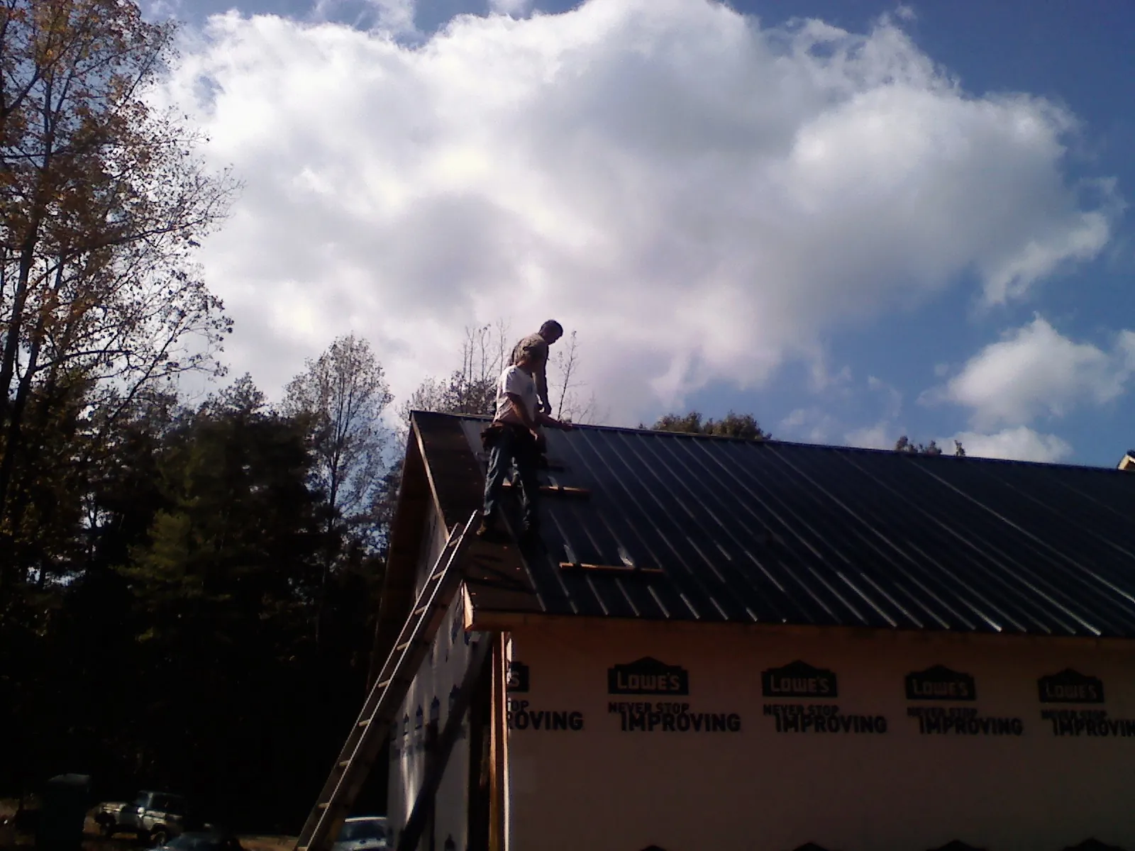 Roofer fastening dark metal panels high against a cloudy sky, from a Roof Inspection job in Madison